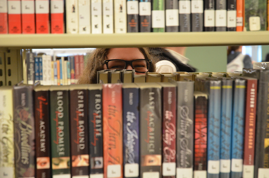 Morgan Hawkins ’19 peeks through the bookshelves in the West High School Library during 7th period. She shares a joyful reunion with her friend, Allie Harvey ’19, after a long day at school.