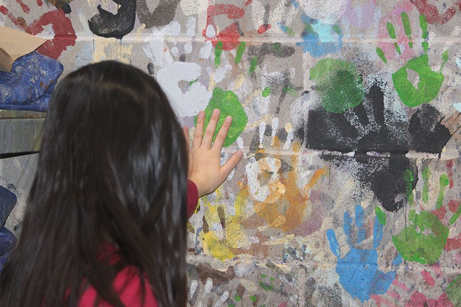 Nina Meng ’21 puts her hand on the wall of colorful handprints in the set designing room. The handprints add a splash of color to the otherwise colorless wall.