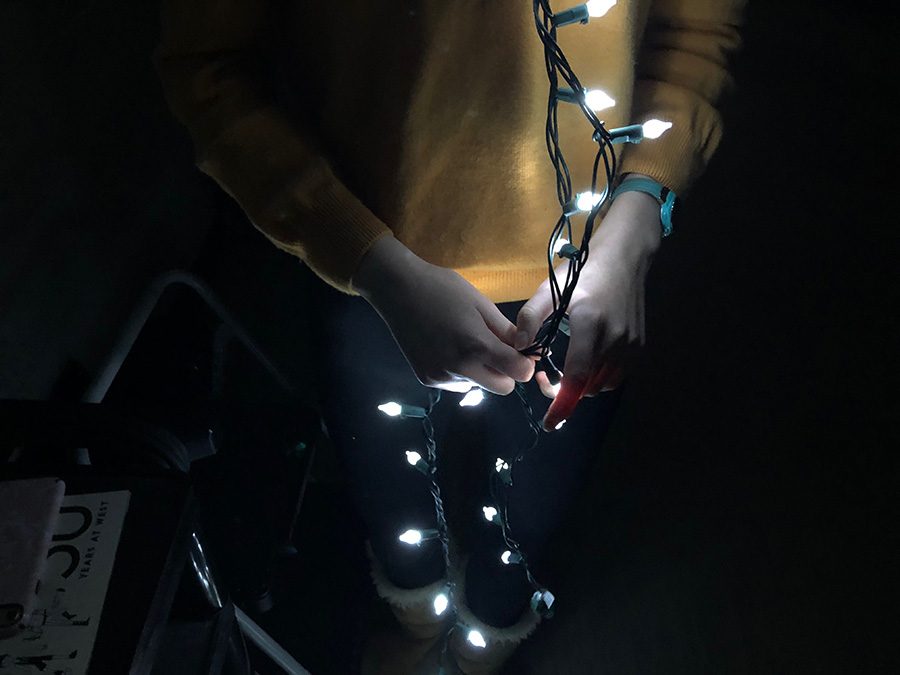 Lily Meng 19 is shown holding a string of Christmas lights by their light illuminating her hands and body. 