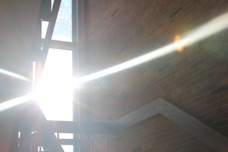 Behind a window, the Sun’s light is fractured into three separate beams of light shooting into the staircase of West High.