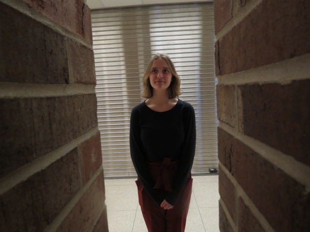 Zoe McLaskey 22 stands behind the brick pillars in the West High commons.  (Framing)