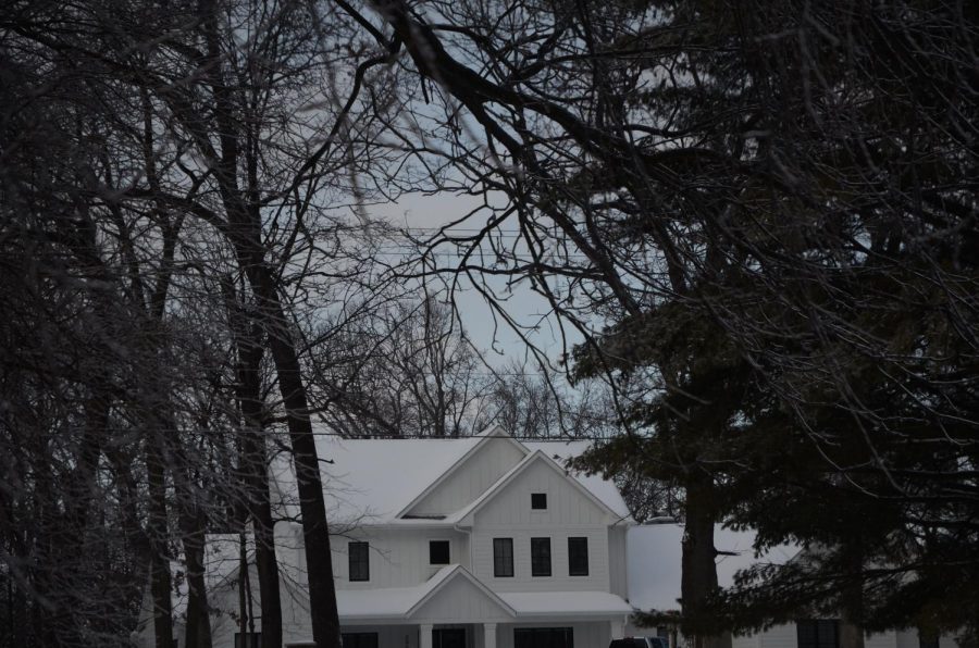 On a chilly, cloudy day, a bright white house stands out from the dark branches of the forest. [Framing & Featured]

