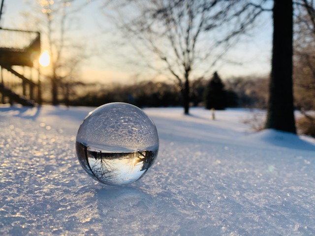 A glass orb sitting on the icy, frozen ground during a beautiful sunset.