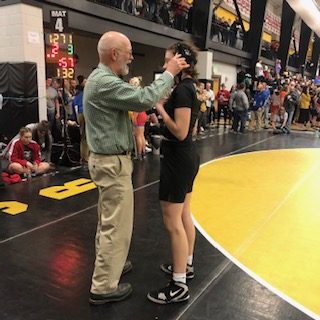 Coach Mike Haverkamp adjusts Emma Dunlap 22s headgear after her wrestling match at the State tournament on Jan. 26th. (Feature)